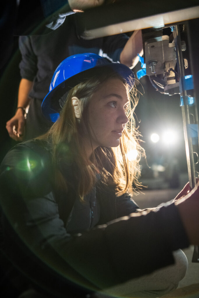 Madeleine Bardy, wearing a blue hardhat, working at night on complex machinery associated with a rocket engine.