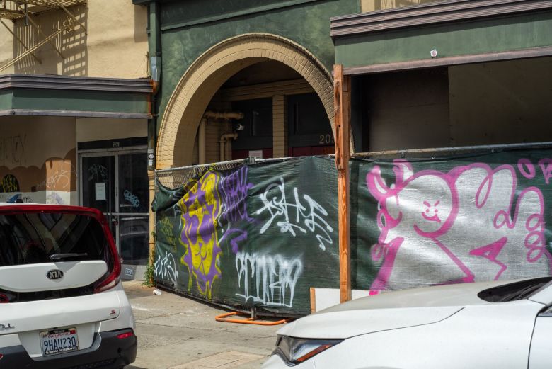 Graffiti-covered fences surround the entryway of an apartment building