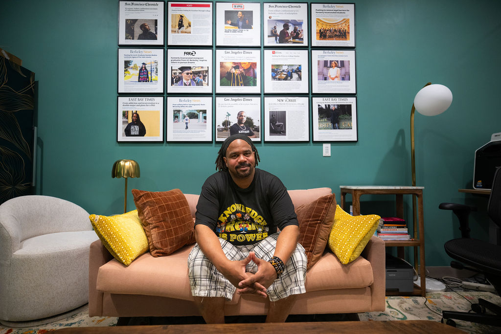 Charles Long seated on a couch in the Underground Scholars office, a space where he has found community during his time at Berkeley. On the wall behind him are news stories chronicling the successes of others who have gone through the program before him.
