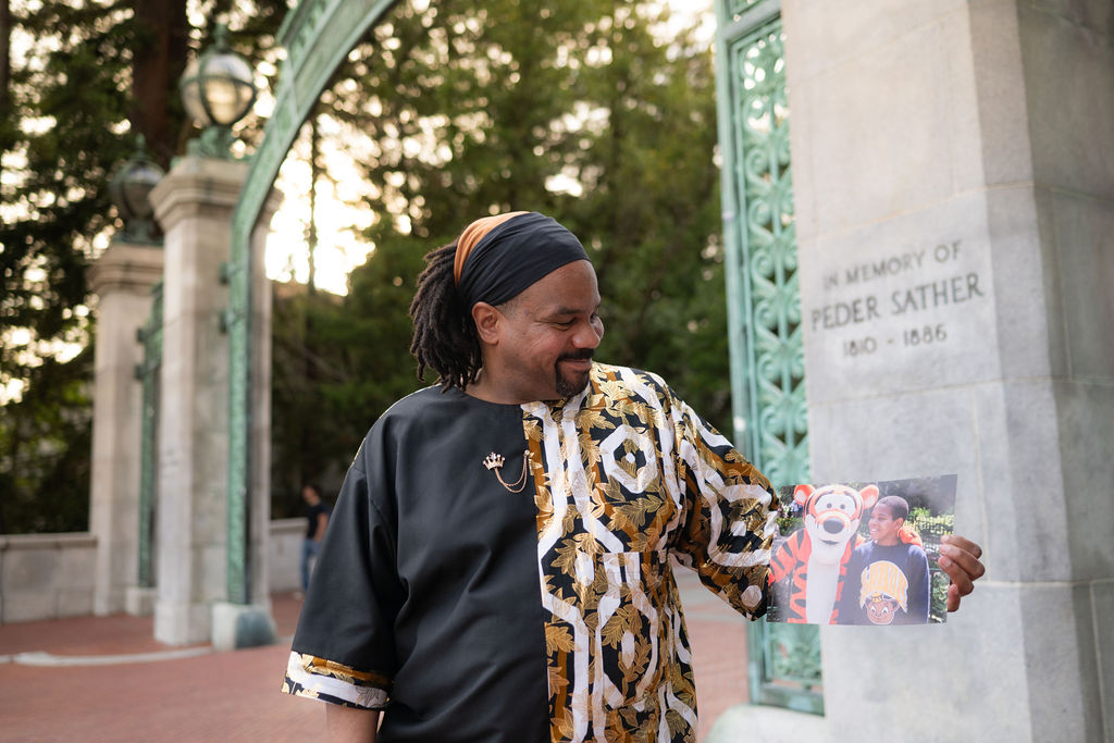 Long stands near Sather Gate, looking at an image of himself as a young boy, wearing a UC Berkeley sweatshirt.