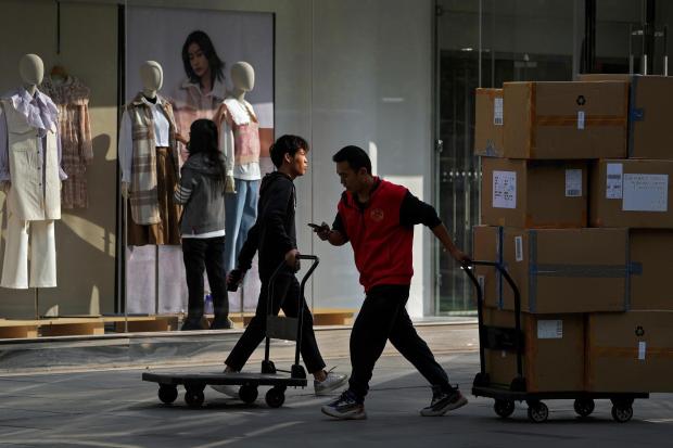 Workers push carts loaded with goods past an employee who adjusts clothing on mannequins.