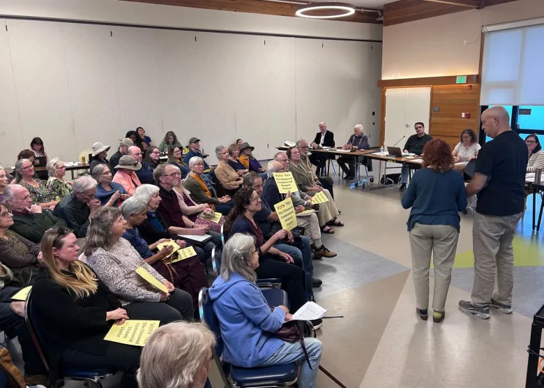 People fill a community meeting, many of them holding signs that read, "vote yes the Elmwood Historic District"