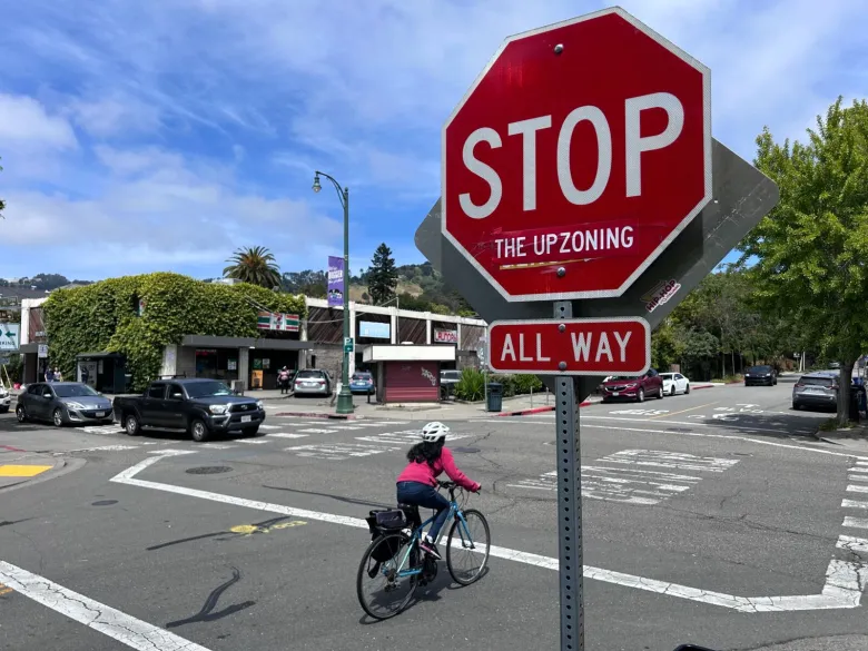 A stop sign where someone has affixed a sticker that reads "the upzoning" stands at abusy intersection