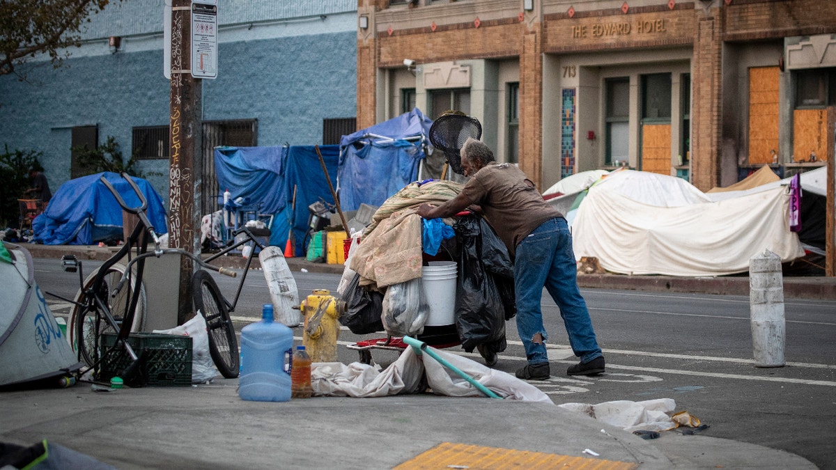 A person pushing a cart through a homeless encampment on Skid Row in Los Angeles