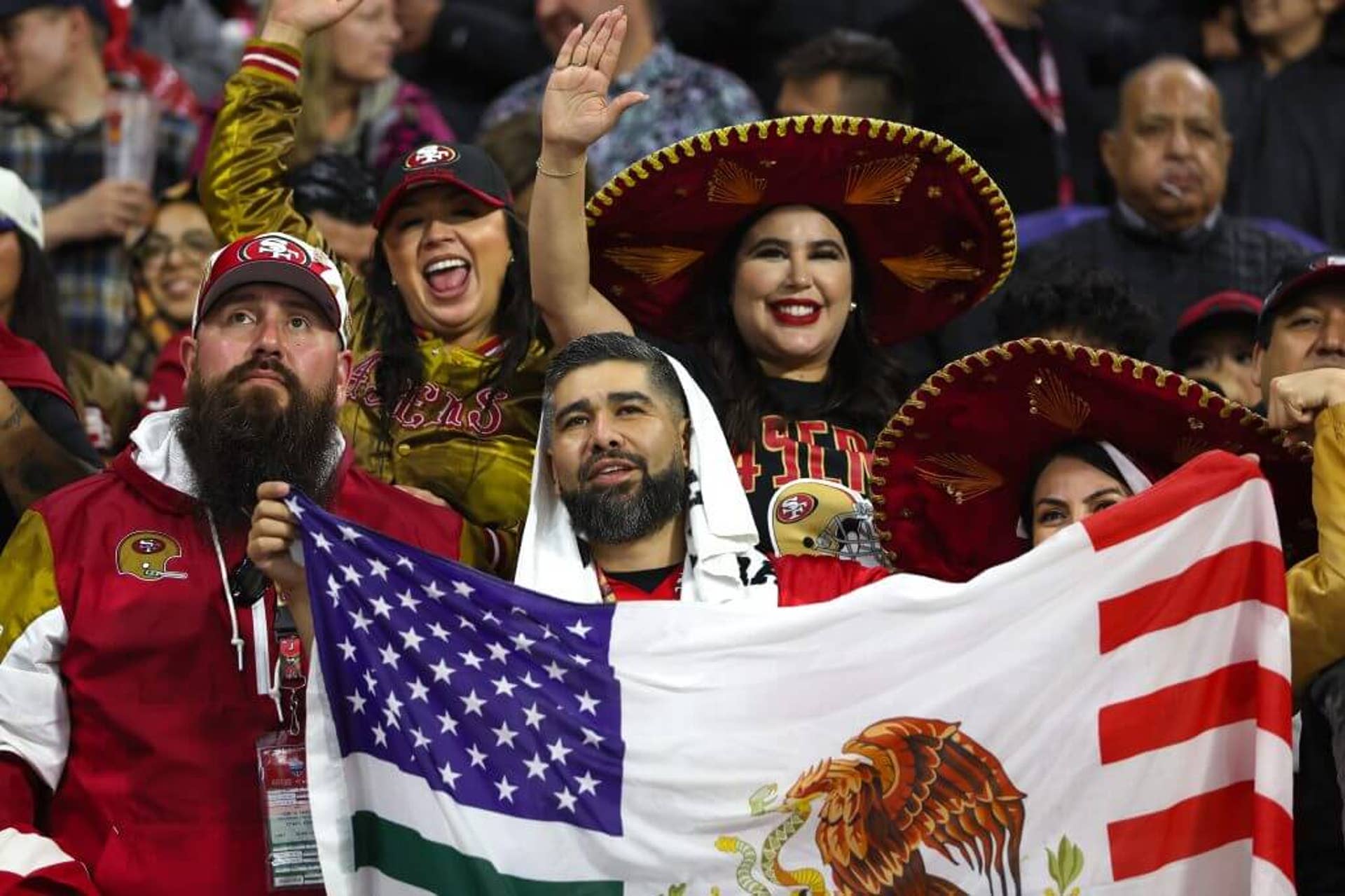 Fans clad in 49ers gear, including two red and gold sombreros, hold up a flag featuring elements of the U.S. and Mexican flags.