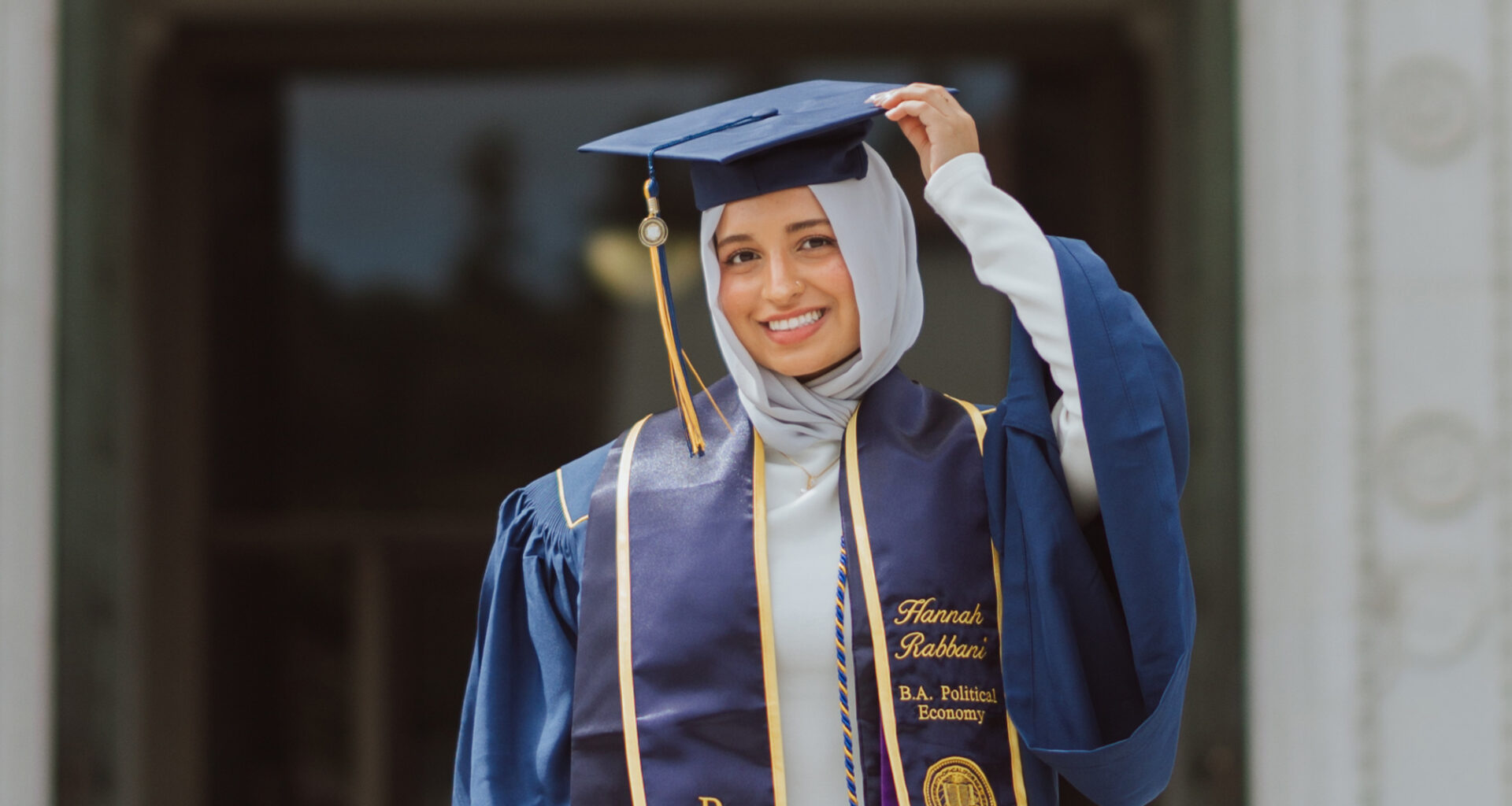 Portrait of Hannah Rabbani in her UC Berkeley graduation regalia. She is wearing a navy gown, a custom stole with her name, and a white hijab.
