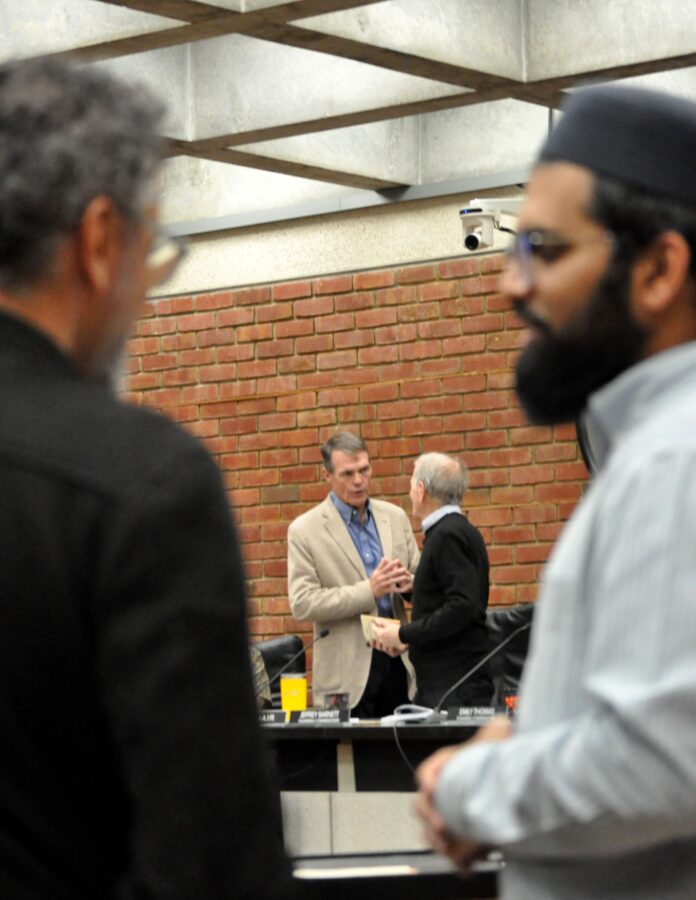 two commissioners speak at break while two Muslim attendees stand in the foreground