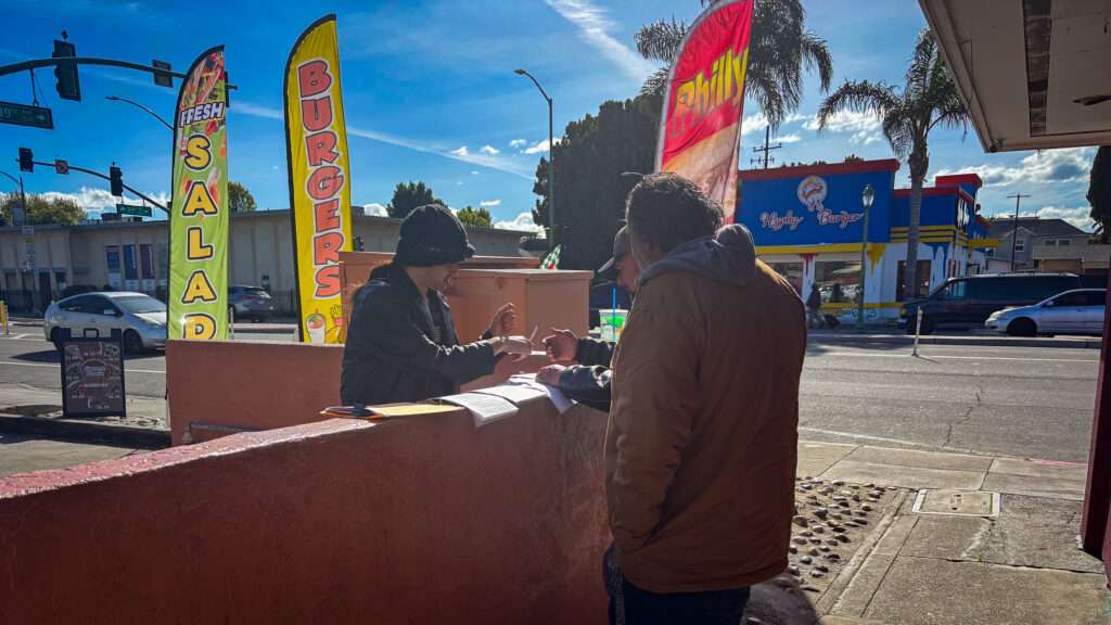 Three men signing documents on top of a low wall near a street.
