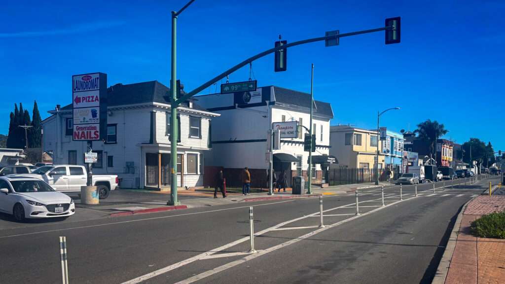A photograph of a street, with two-story white buildings on the other side of it.