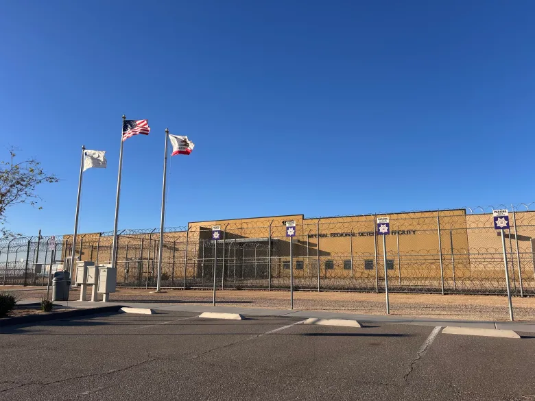 A fenced building with flags in front under a clear blue sky.