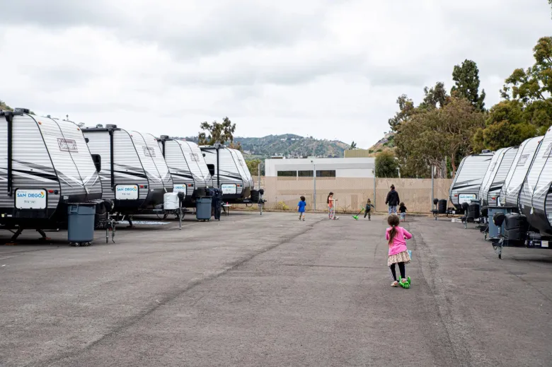 Rows of RV trailers with children playing on scooters in a lot.