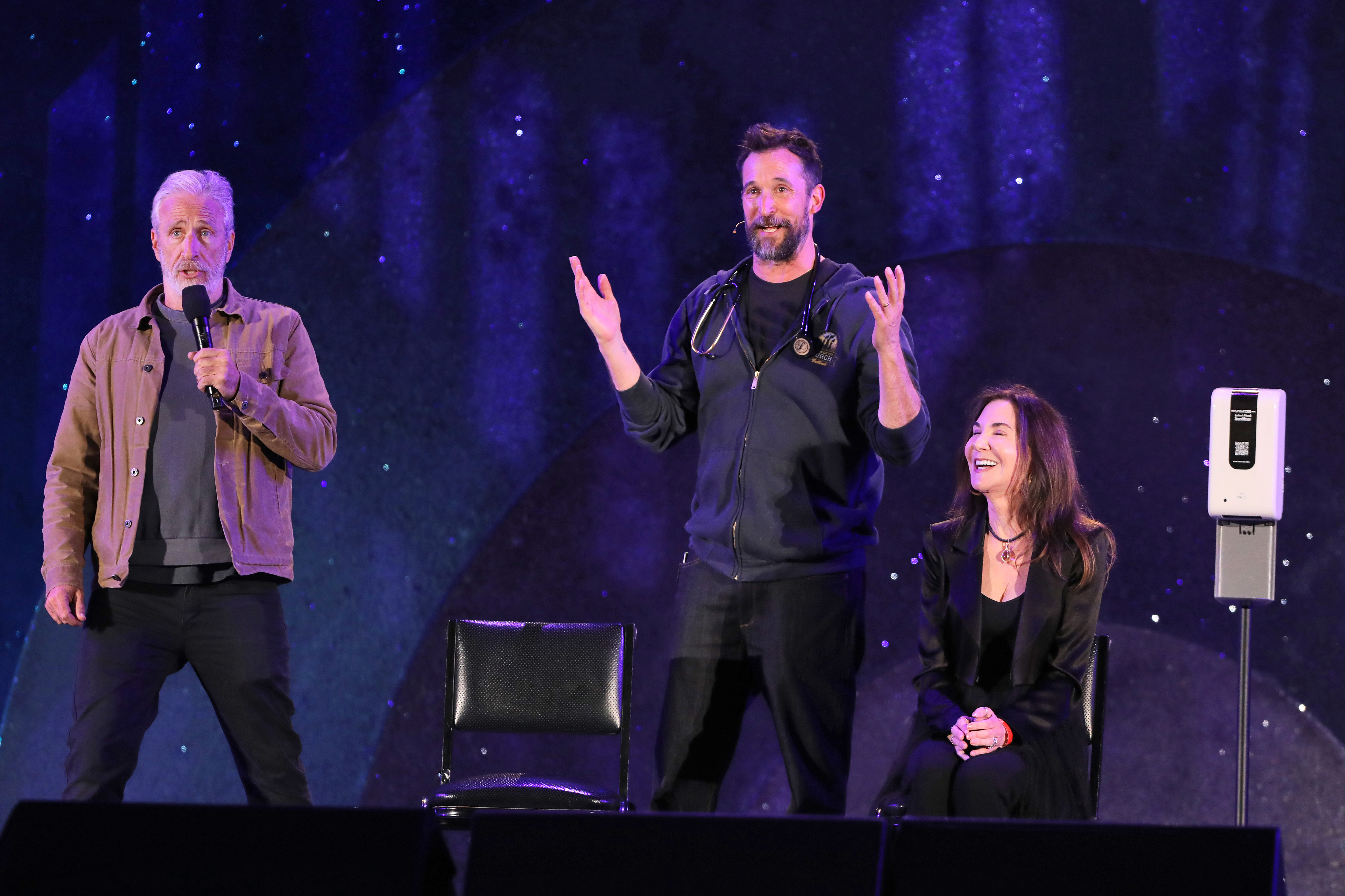 Jon Stewart, Noah Wyle, and a bidder share the stage...