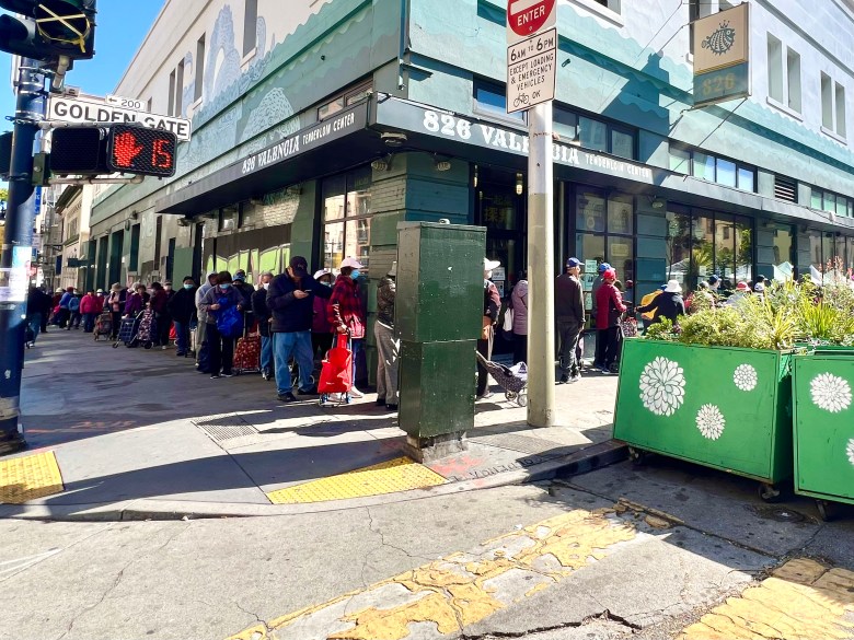Line wraps around a building outside as people wait to get groceries
