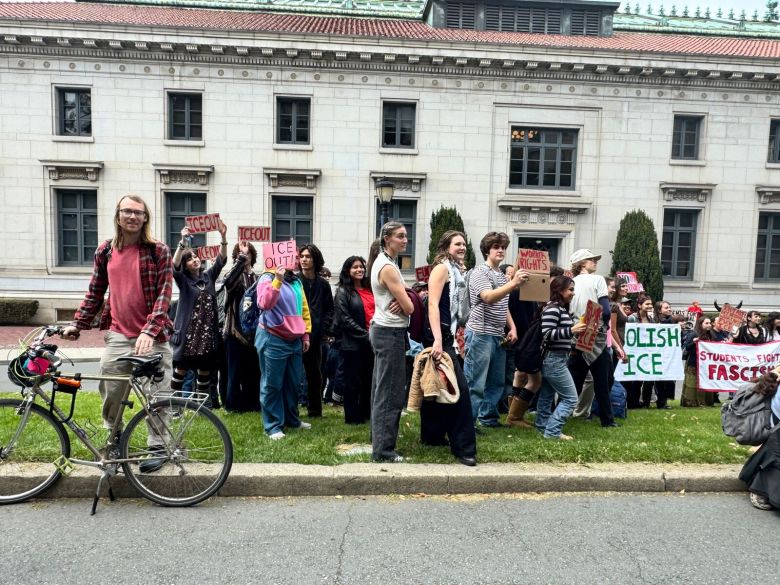 A group of young people stand on a lawn, many of them holding protest signs