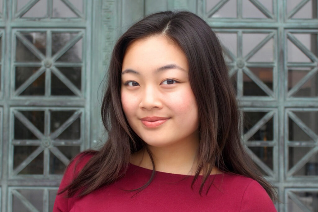 headshot of Mye Pinmada Makornwattana, wearing a burgundy-colored shirt and standing against backdrop of geometric forms in green-hued oxidized copper.