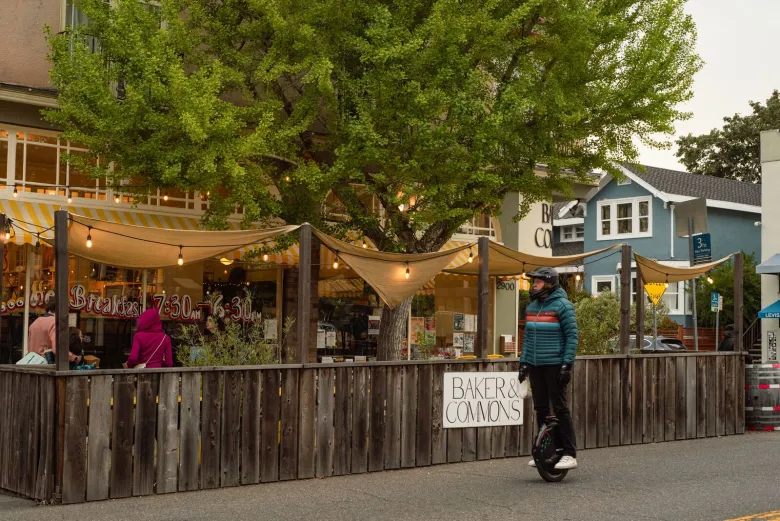 A person rides past the attractive parklet for the restaurant Baker and Commons, which is decorated with string lights and shades