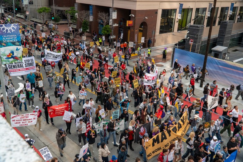 A view of a large march from above the street, with people holding a sign saying "May Day"