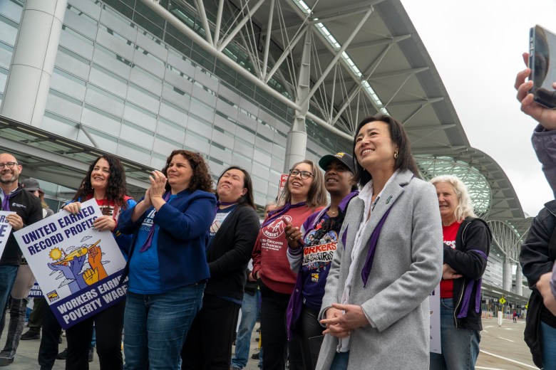 A group of people, including Supervisor Connie Chan, stands in front of a large modern building