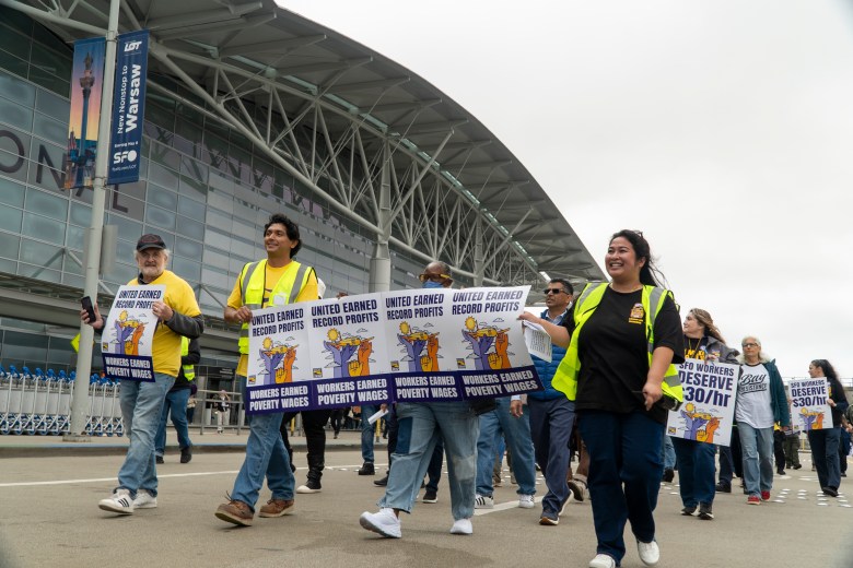 A line of marchers in front of an airport terminal hold signs saying "United earned record profits, workers earned poverty wages"