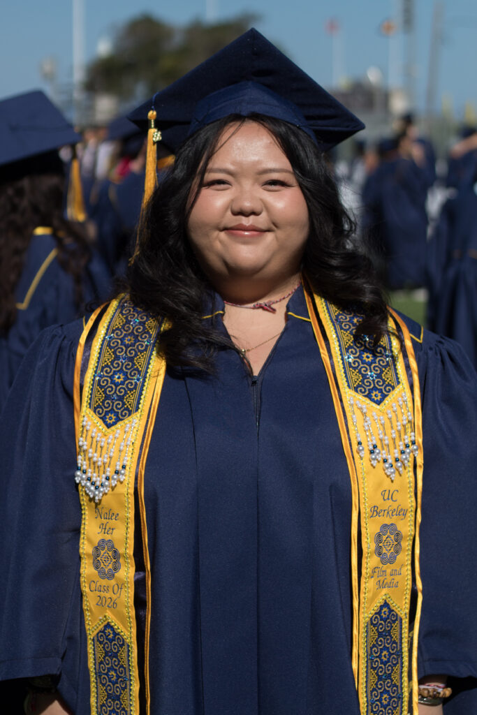 A woman wearing a blue gown and embroidered yellow stole smiles at the camera
