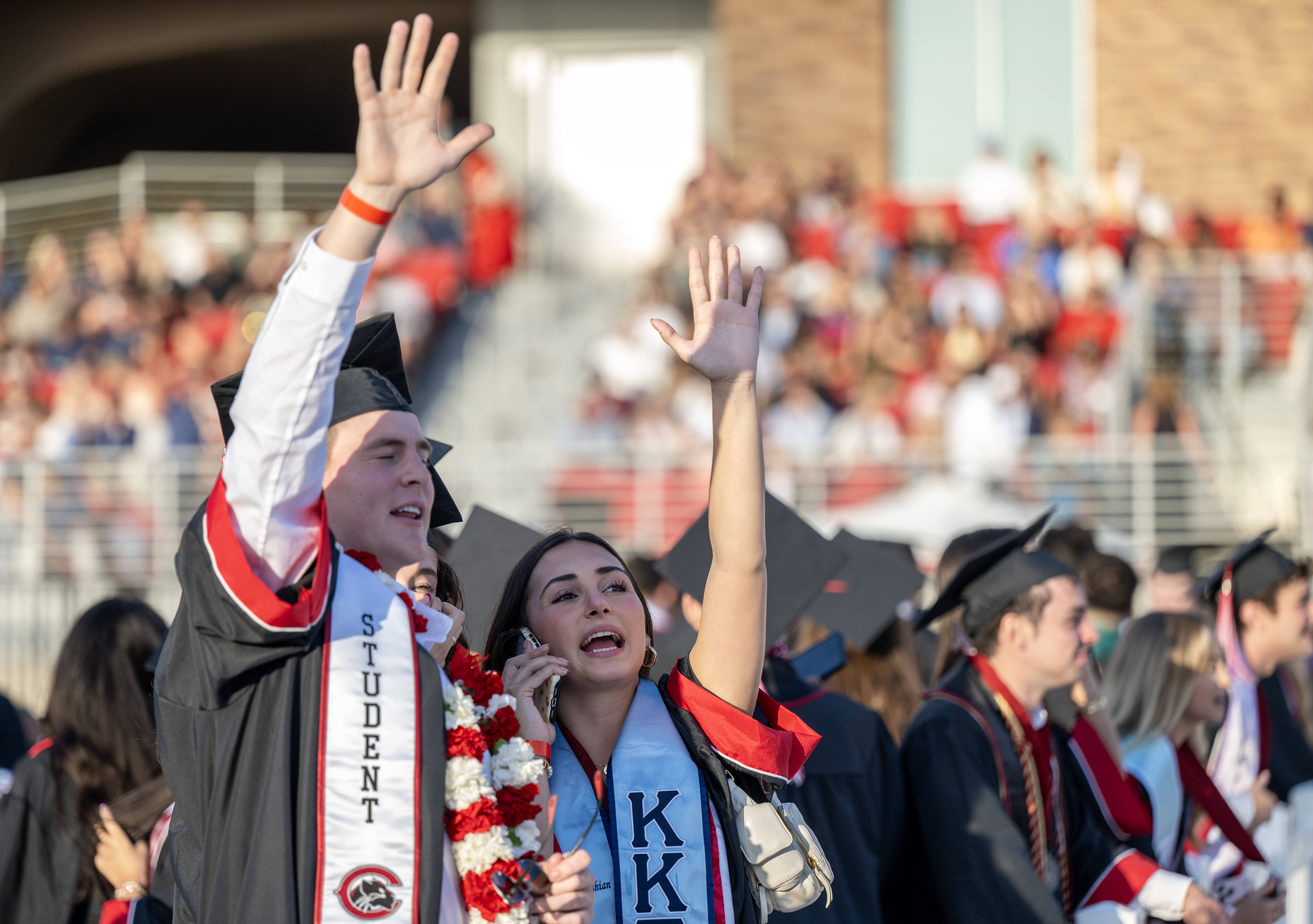 Graduates wave to their loved ones in the stands as...