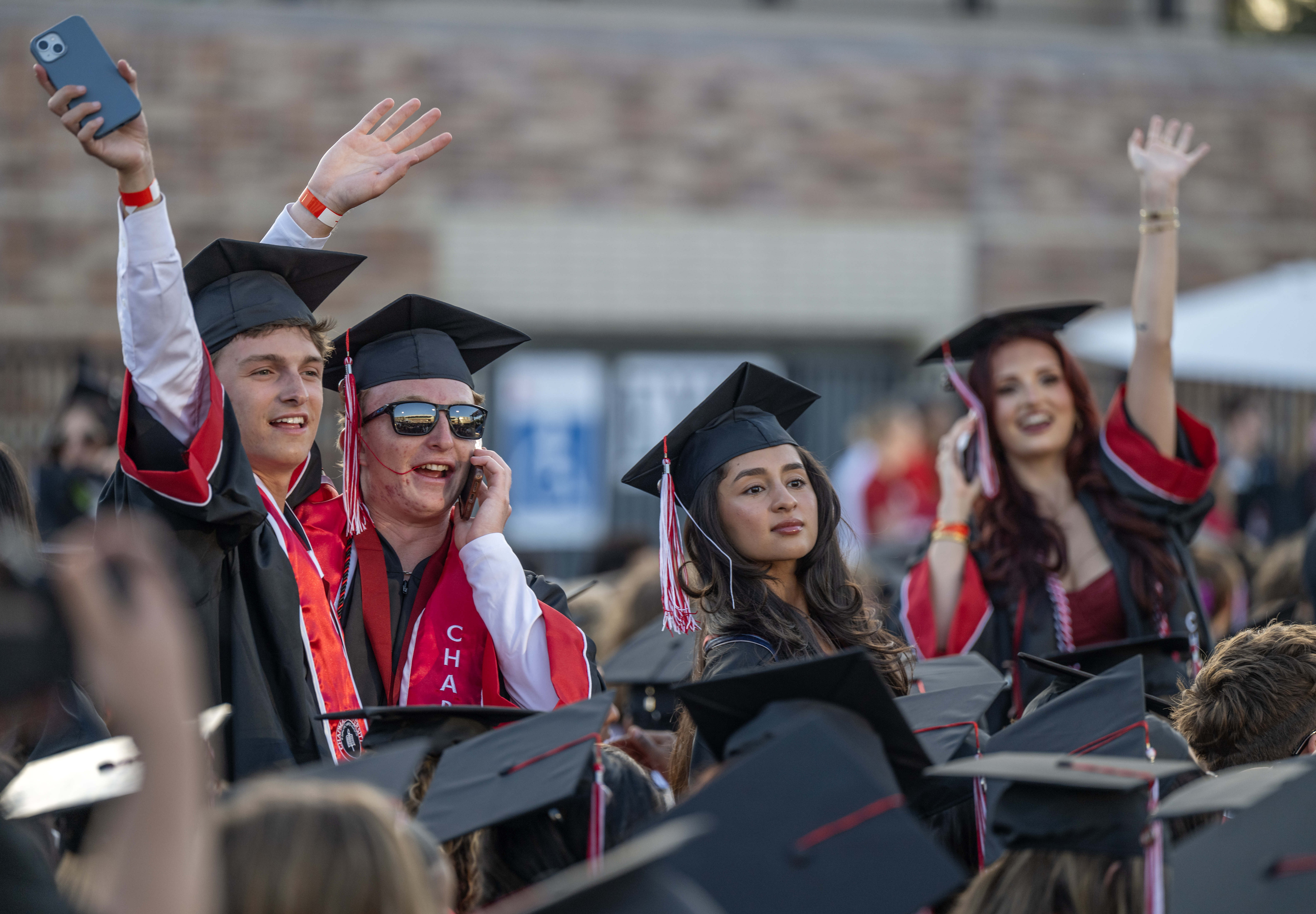 Graduates wave to their loved ones in the stands as...