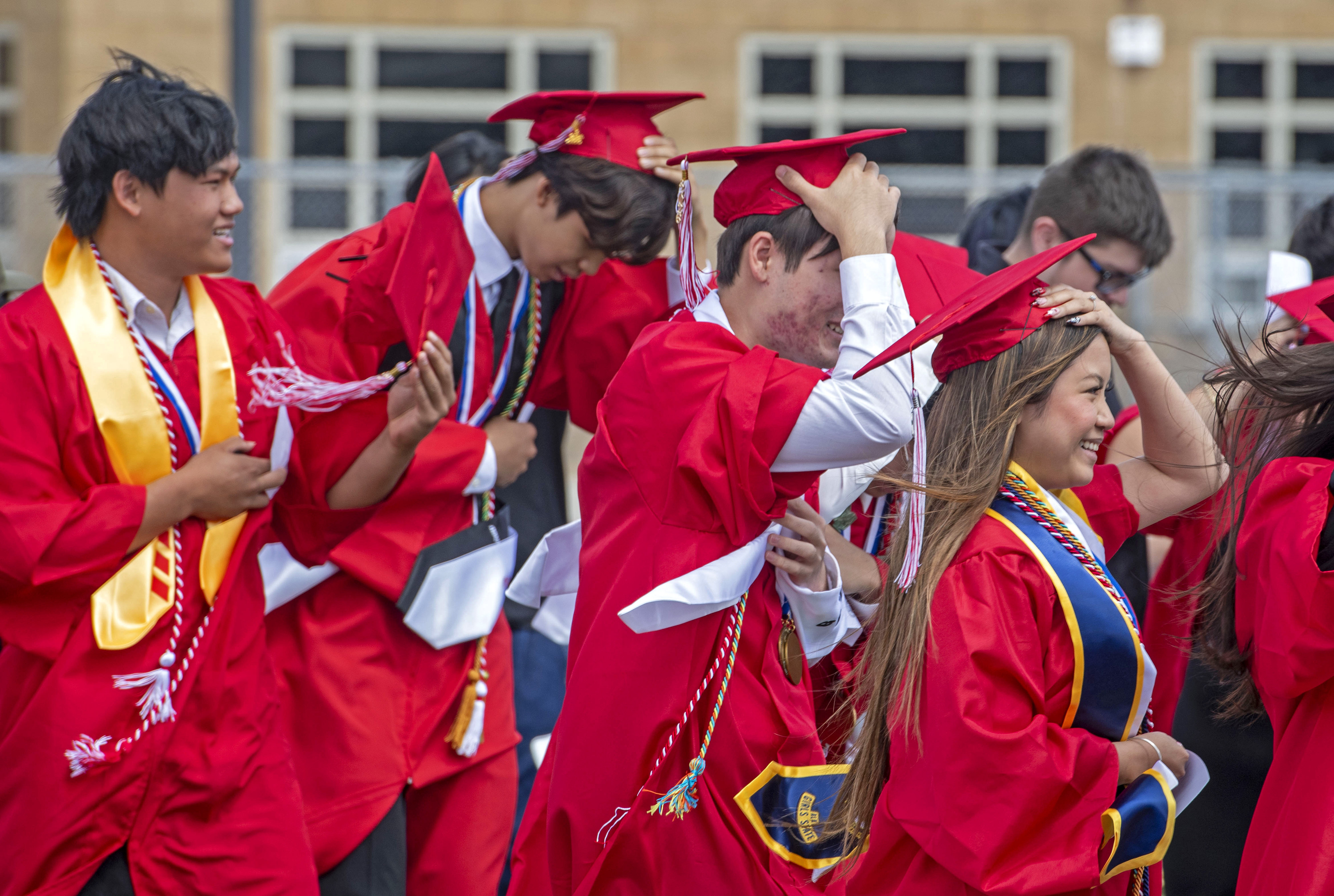 Graduates struggle to keep their hats on during a blustery...