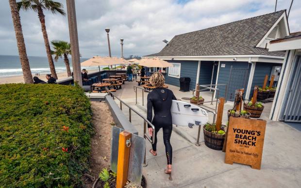 A surfer walks past the entrance to Young's Beach Shack, a new beachfront eatery, which opened at Salt Creek Beach in Dana Point on Tuesday, February 21, 2023, after nearly a year of construction. (Photo by Mark Rightmire, Orange County Register/SCNG)