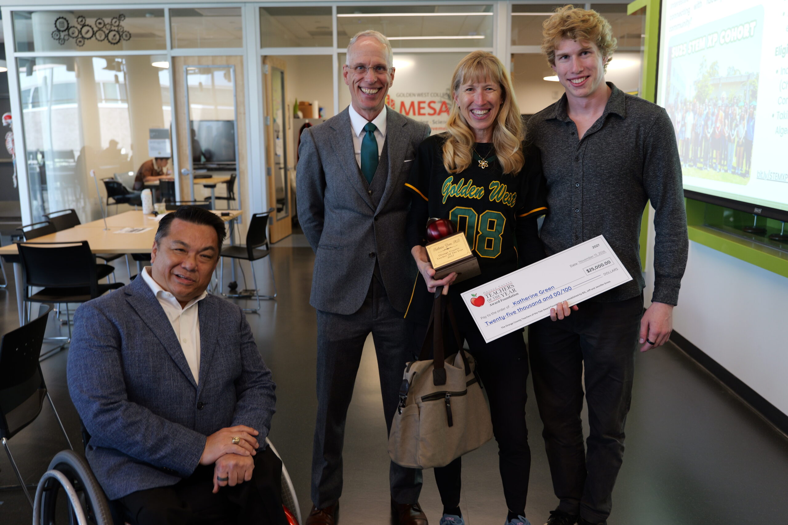 Dr. Katherine Green, a Golden West College professor, poses with her husband, son and Orange County Superintendent of Schools Dr. Stefan Bean after being surprised as a 2027 Orange County Teacher of the Year. Green holds her award check, apple-shaped trophy and a gift bag from SchoolsFirst Federal Credit Union.