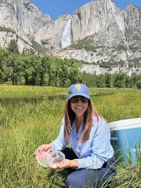 Woman holding frog next to river. CDFW photo