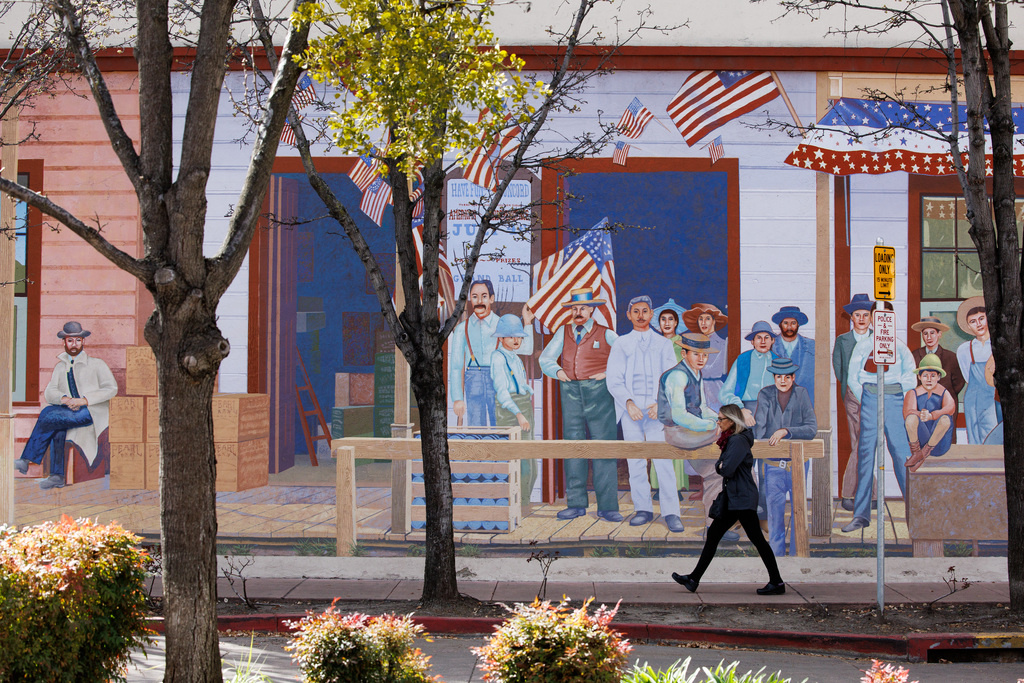 A pedestrian walks by a mural depicting a Fourth of...