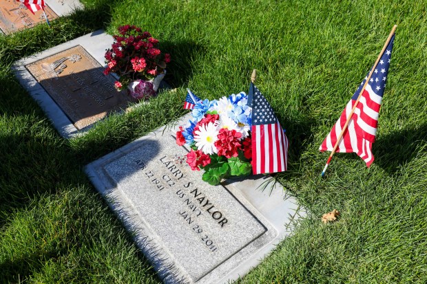 American flags stand in front of the gravestones of fallen soldiers as Conni Naylor stands by the gravestone of her husband, Navy veteran Larry Naylor, at Memory Garden Cemetery in Livermore, Calif., Saturday, May 23, 2026. About 120 mother-and-son teams from the Livermore chapter of the Young Men's Service League, in partnership with members of American Legion Post 47, placed the American flags for Memorial Day weekend at Memory Garden Cemetery and St. Michael's Cemetery. (Ray Chavez/Bay Area News Group)