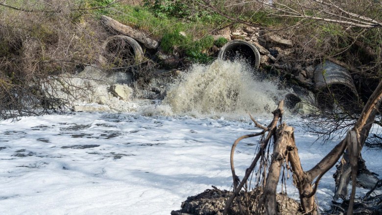 A barrage of what looks to be tainted water pours from a drainage pipe into a body of water.