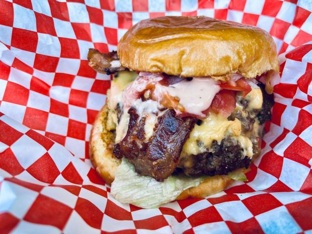 The Coach at Average Joe Burgers contains American cheese, bacon, tomatoes, pickles, lettuce, red onions and a secret sauce. (Carlos Rico / The San Diego Union-Tribune)