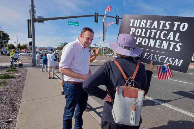 Brandon Riker, left, greets one of the many people demonstrating against Rep. Darrell Issa and President Donald Trump at the busy intersection of Broadway and E. Lincoln Parkway in Escondido on Dec. 12, 2025. (Charlie Neuman / For The San Diego Union-Tribune)