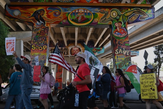 People gathered with flags and signs for a May Day rally marking International Workers Day at Chicano Park in the Barrio Logan neighborhood of San Diego on Friday. (Carlos Moreno / The San Diego Union-Tribune)