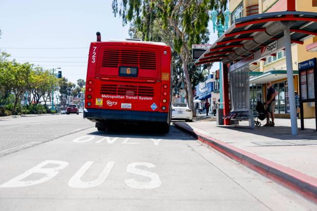 People wait at a bus stop along El Cajon Boulevard on Friday, May 8, 2026, in San Diego, California. (Meg McLaughlin / The San Diego Union-Tribune)