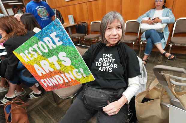 Kaylan Thornhill holds a poster asking city officials not to cut arts funding at a budget hearing at City Hall on Wednesday, May 27, 2026. (Michael Ho / For The San Diego Union-Tribune)