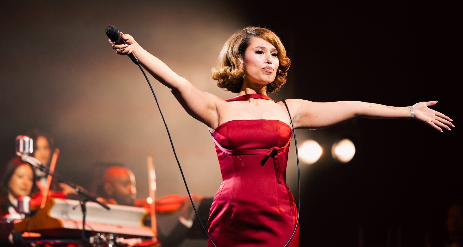 Raye holds a microphone in a red gown as she performs onstage.