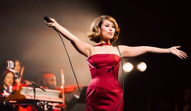 Raye holds a microphone in a red gown as she performs onstage.
