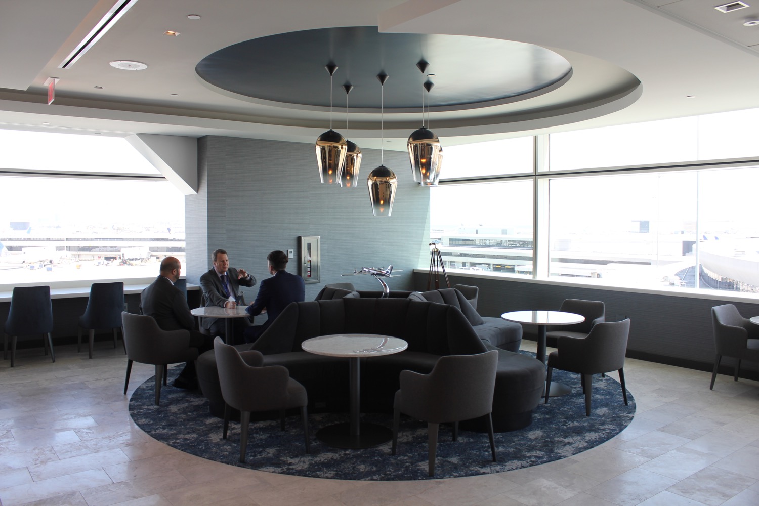 a group of men sitting around a round table in a room with windows
