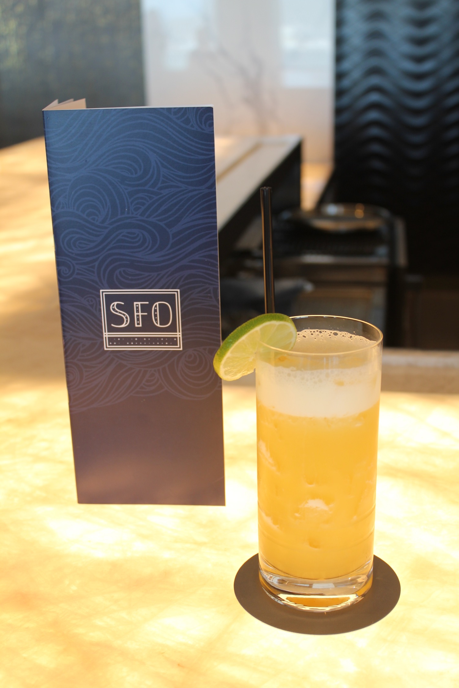 a glass of orange liquid with a straw and lime wedge
