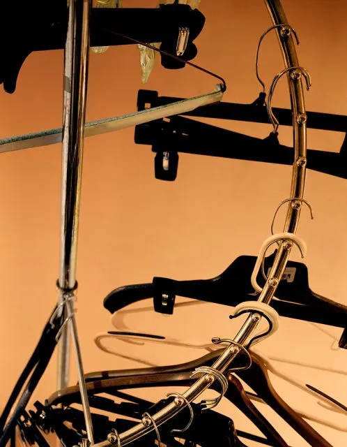 A close-up of several empty black and beige clothes hangers hooked onto a circular metal rack against an orange background.