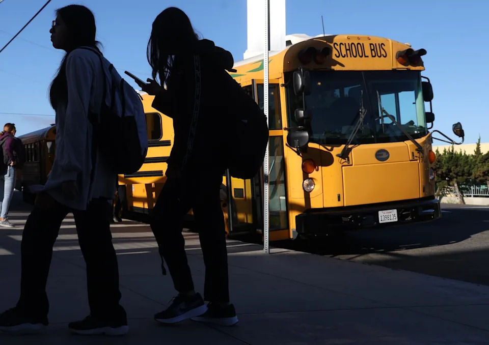 Two people walk near a yellow school bus.