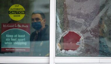 A police officer works behind a broken glass door at the scene where two people were struck by gunfire in a shooting at the Burlington Coat Factory store in North Hollywood, Calif., Thursday, Dec. 23, 2021. (AP Photo/Ringo H.W. Chiu)