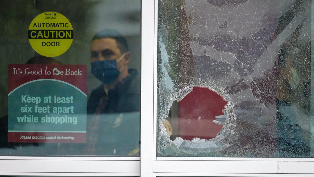 A police officer works behind a broken glass door at the scene where two people were struck by gunfire in a shooting at the Burlington Coat Factory store in North Hollywood, Calif., Thursday, Dec. 23, 2021. (AP Photo/Ringo H.W. Chiu)