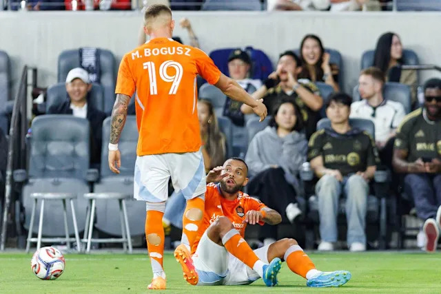 Guilherme Augusto #20 of Houston Dynamo FC gets helped up by Mateusz Bogusz #19 during an MLS match against LAFC on May 10, 2026 at BMO Stadium in Los Angeles, California.