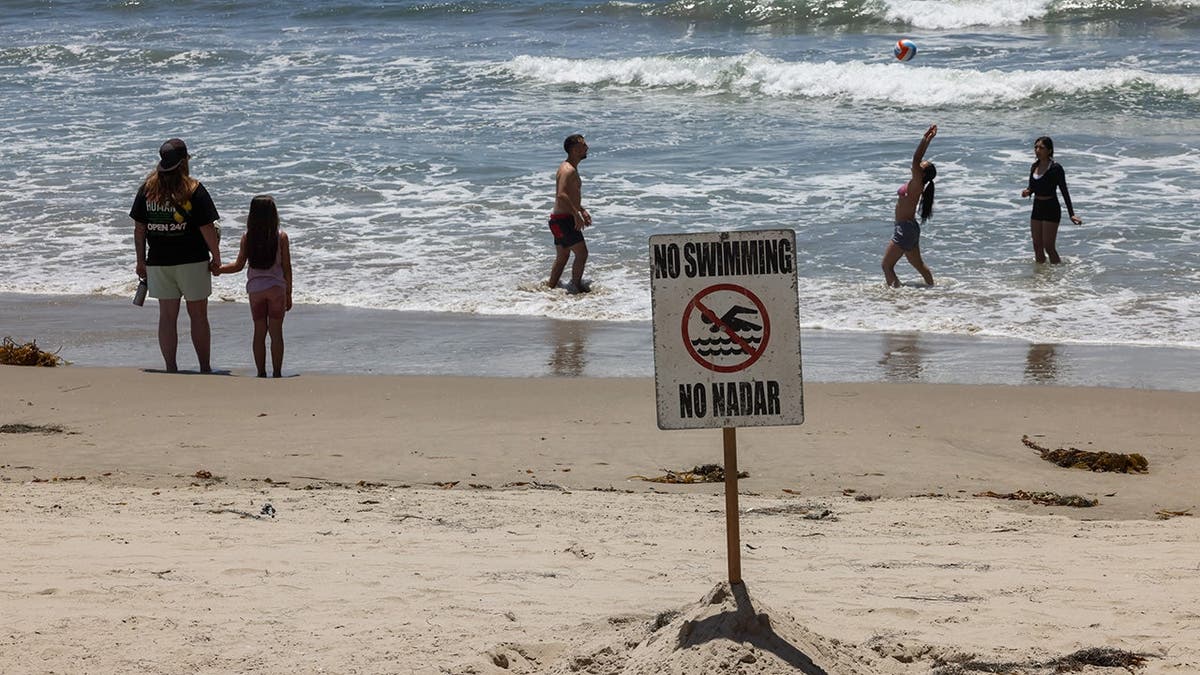 A few people frolic in the ocean water of a Santa Monica Pier beach near a No Swimming sign.