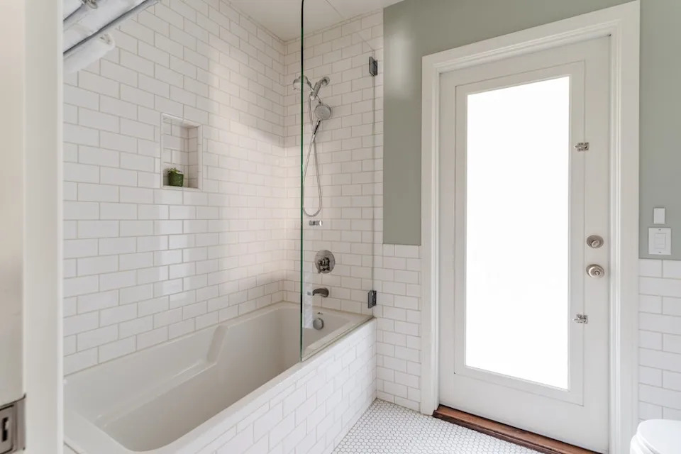 A bright bathroom featuring a white subway-tiled bathtub and shower combination with a glass partition.