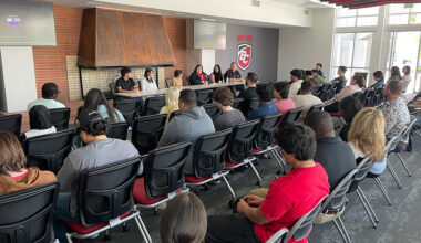 student panelists sitting at a table facing a medium sized audience; BC logo in the back